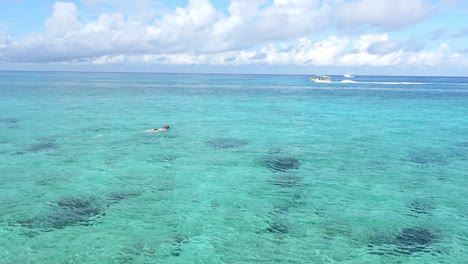 A-women-snorkeling-in-the-clear-tropical-waters-of-Cozumel-Island,-Mexico-as-a-motorboat-travels-by-in-the-background