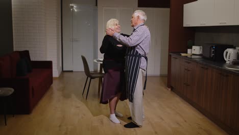 Pareja-De-Ancianos-Enamorados-Tienen-Una-Velada-Romántica,-Bailan-Juntos-En-La-Cocina,-Celebran-El-Aniversario