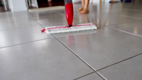 a red spray mop glides over a tiled floor, enhancing cleanliness with water spray. bright lighting highlights the cleaning process