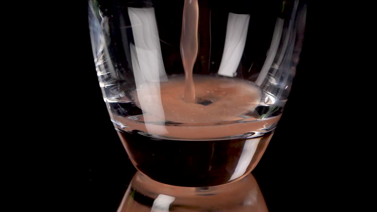 Versare succo di pompelmo in un bel bicchiere al rallentatore su sfondo nero.
