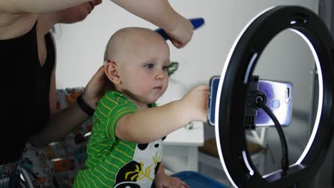 madre cortando el cabello de un hijo pequeño con un cortador de cabello en la cocina.