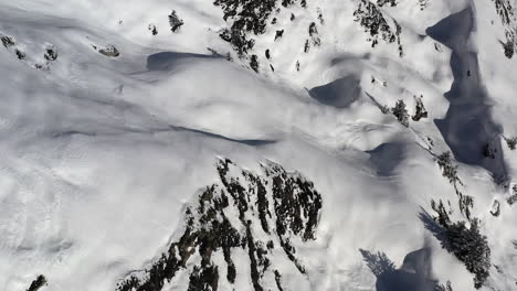 drone shot looking straight down onto a fresh snow covered terrain, then tilting up to reveal ski pistes and a mountain, in la plagne , france