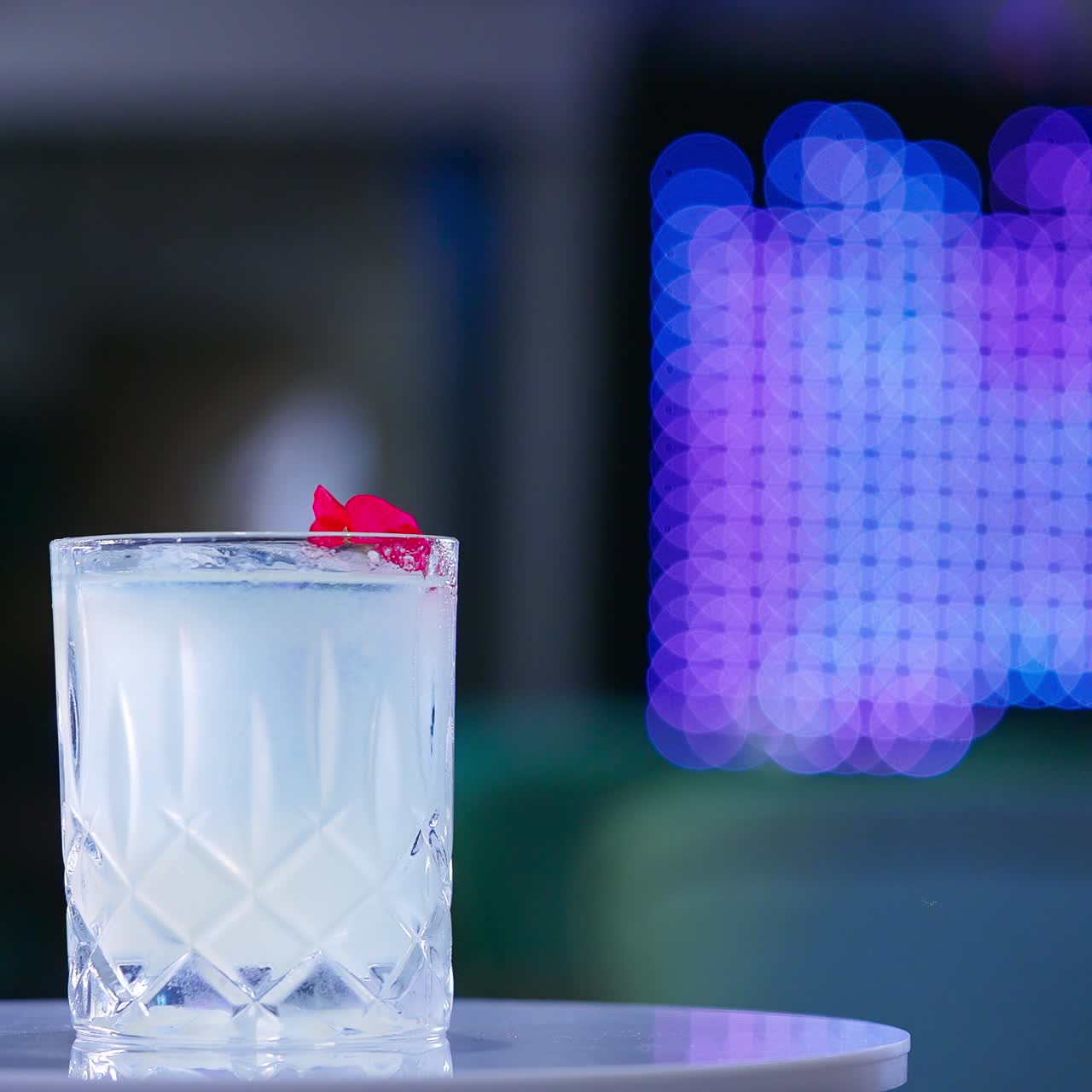 Old-fashioned glass with drink on the rotating table. Cocktail decorated with red flower in the bar. Close up. Blurred backdrop