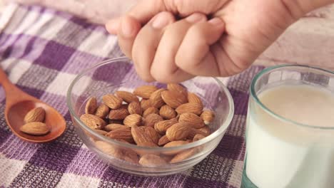 hand picking almonds with a glass of almond milk