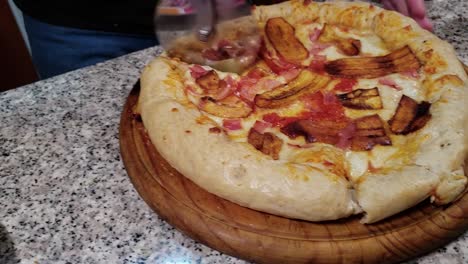 Chef-cutting-a-pizza-with-plantain-and-ham-with-a-wheel-cutter