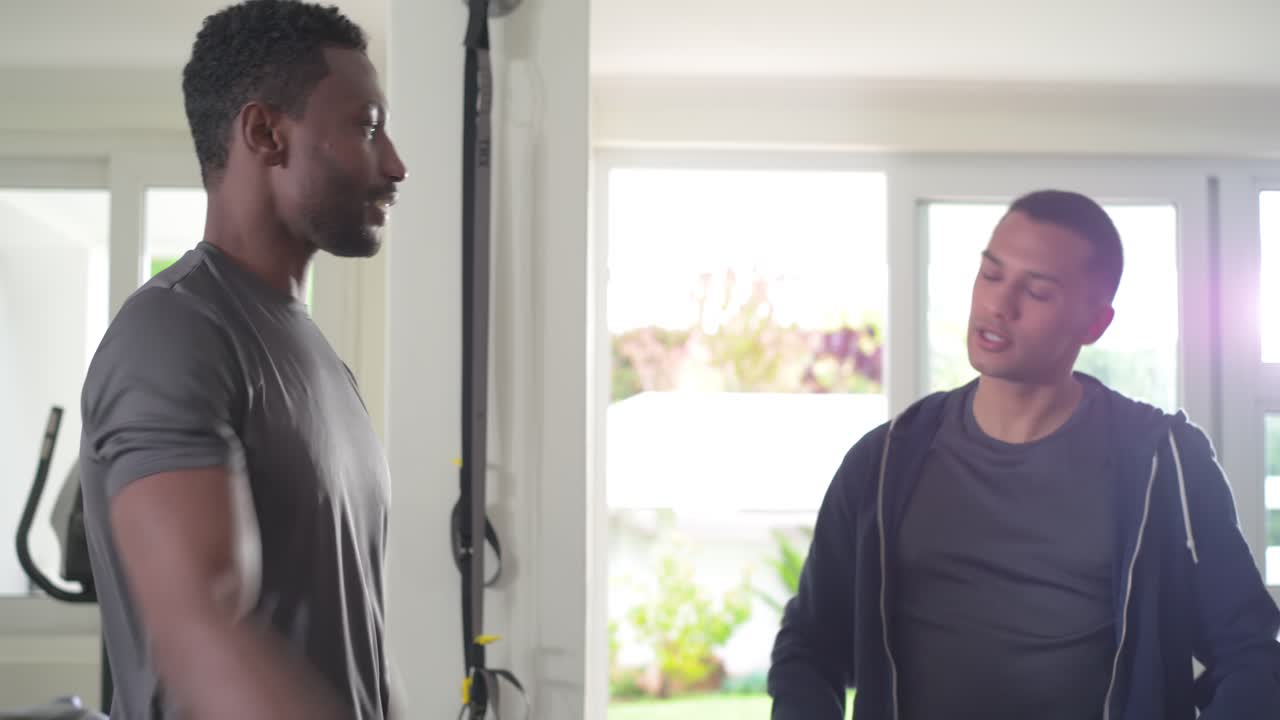 Treinador e cliente afro-americanos se cumprimentando, alongando a parte superior do corpo perto de faixas para aquecimento em casa.