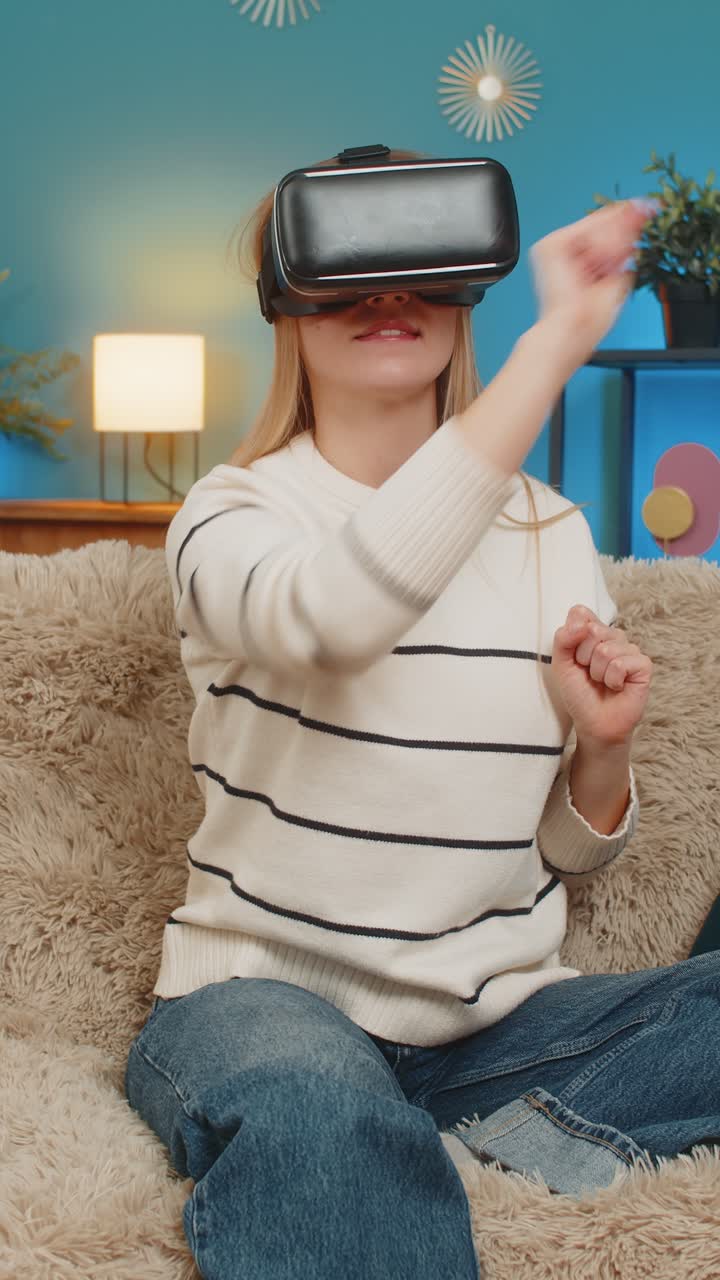 Donna caucasica che gioca a un coinvolgente gioco di realtà virtuale a casa sul divano, gesticolando sorpresa ed entusiasmo in interni