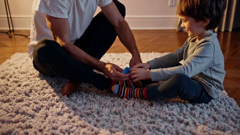 father helping his son put on colorful socks at home