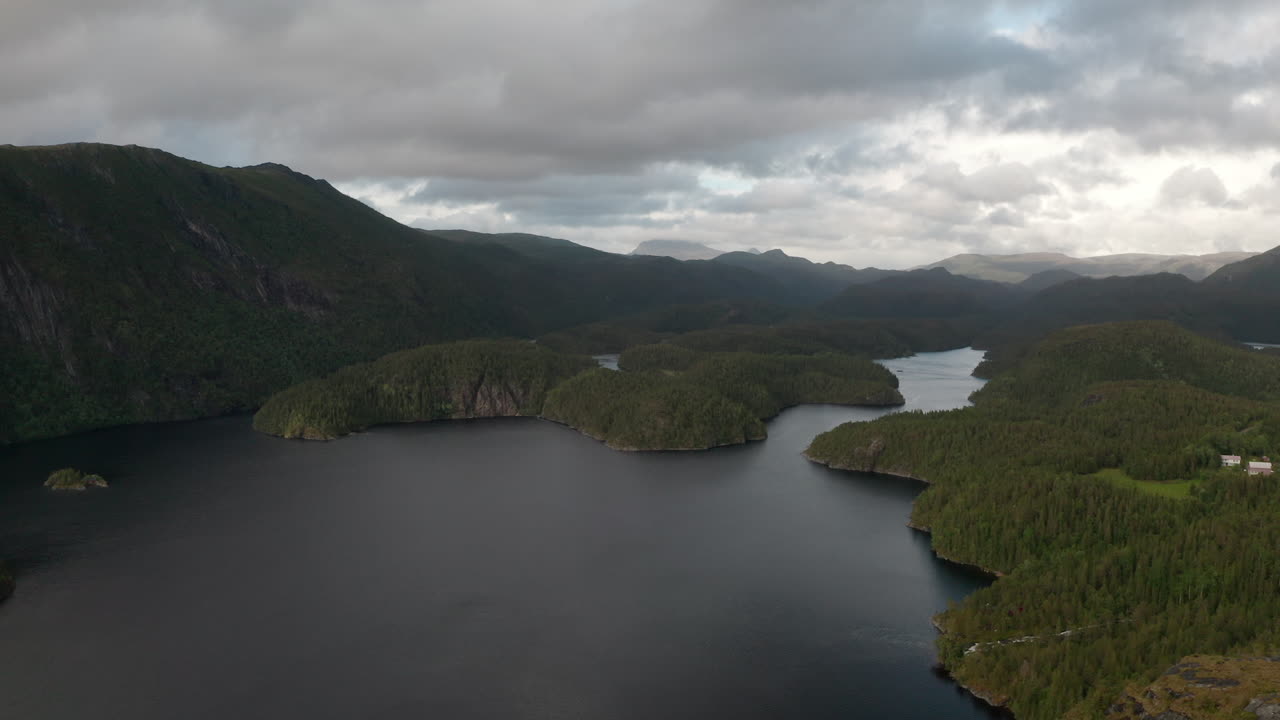 Slow drone footage moving across moody lake with forested terrain and distant mountain peaks
