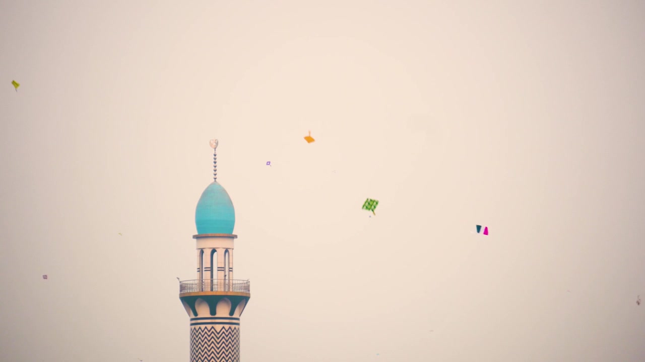 A mosque minaret rises into the sky while kites fly, showing an everyday urban cultural scene