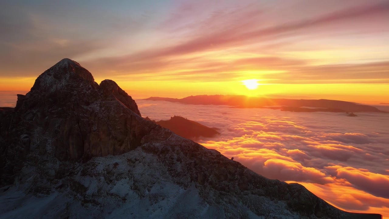 Vista Aérea de Pico de Montanha Coberto de Neve Acima de Mar de Nuvens ao Pôr do Sol