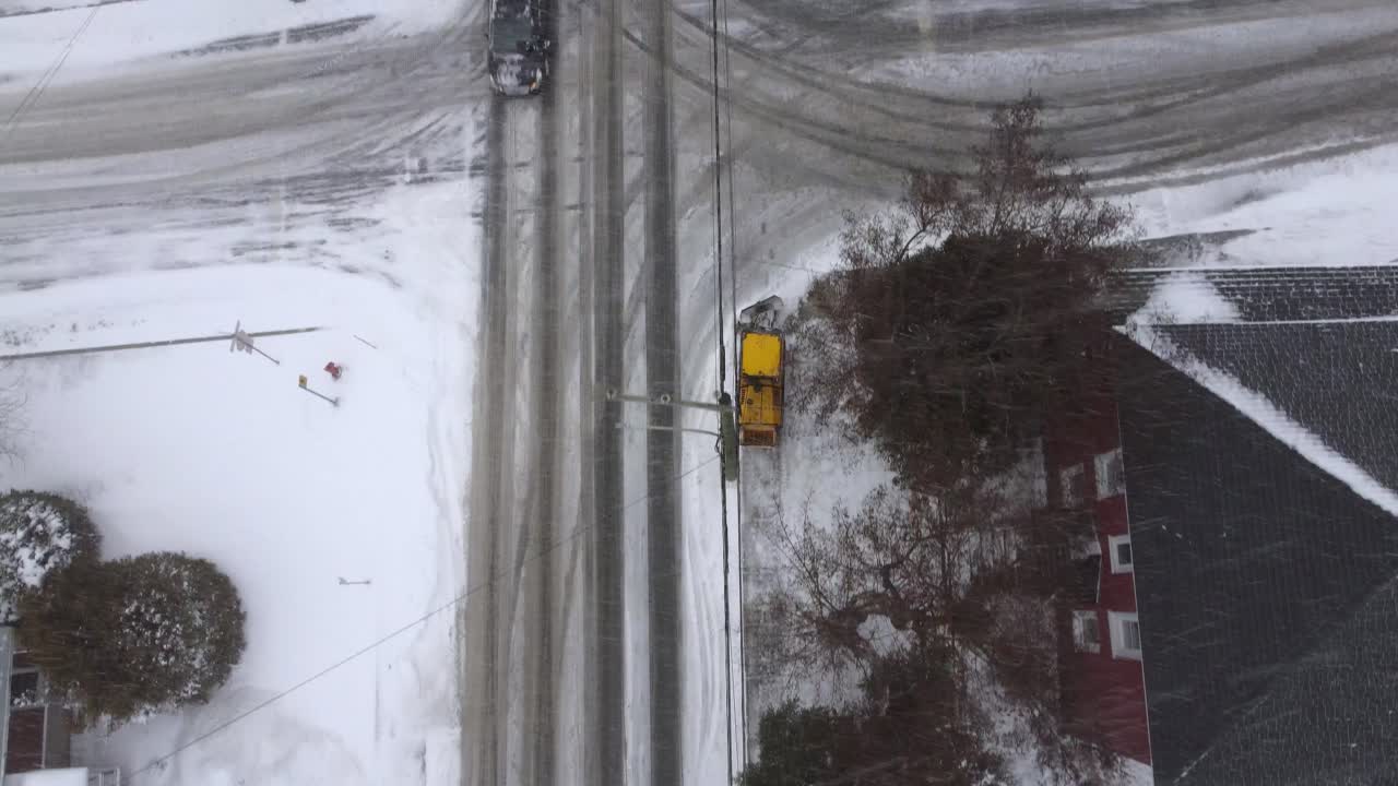 Aerial view of a snowplow clearing a snowy road in a residential area of Orford, Quebec, Canada, during the winter season, providing essential snow removal services, top down drone shot