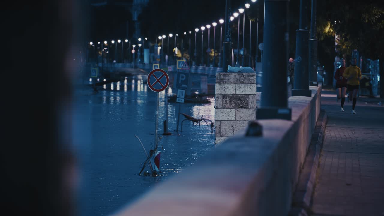 flooded street along the riverside of Budapest with signs submerged, illuminated by streetlights