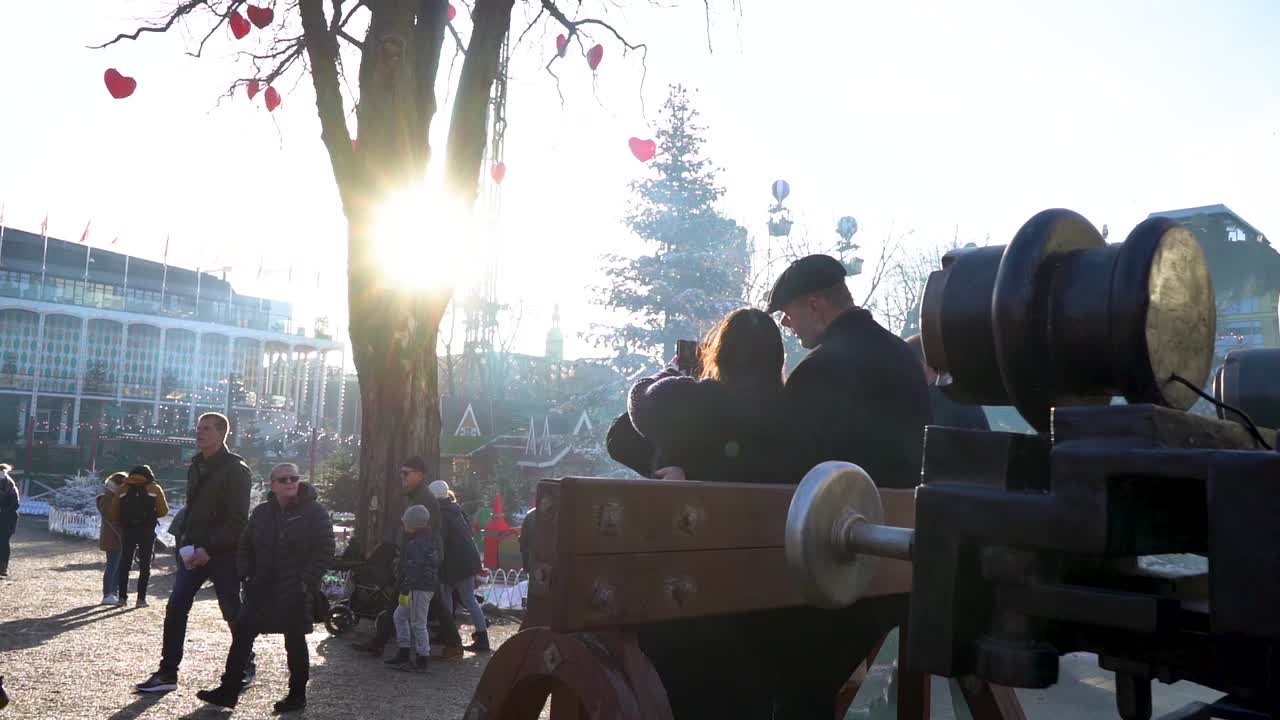 Bright white sun beams shine through branches in decorated tree by people walking, Copenhagen, Denmark, slow motion