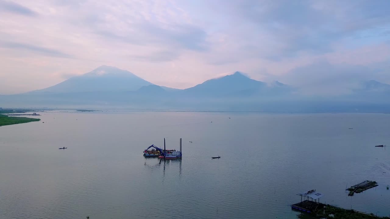 vista aérea del barco dragador con excavadora en el enorme lago con vistas a la montaña en el fondo - lago rawa pening, indonesia