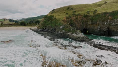 Aerial-reversing-over-rough-and-wild-cliff-coastline-with-white-wash-waves-breaking-against-rocks-in-Cannibal-Bay-in-the-Catlins,-South-Island-of-New-Zealand-Aotearoa