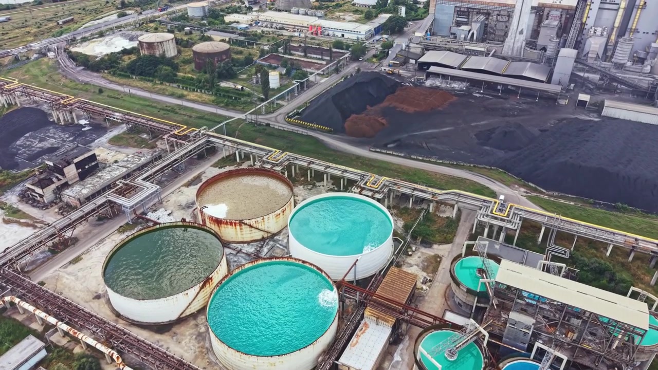 Large industrial site with multiple circular tanks and surrounding infrastructure in an urban area during daytime
