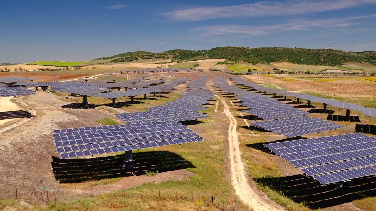 Filmato cinematografico con drone che sorvola un grande impianto fotovoltaico con pannelli che generano elettricità pulita e rinnovabile. Infrastruttura energetica sostenibile a supporto della transizione energetica globale.
