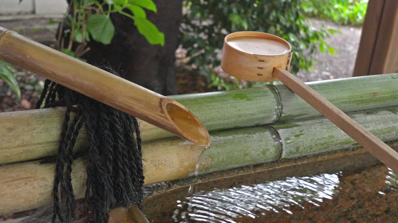 A traditional Chozuya (purification fountain) at Kuramae Shrine, featuring a bamboo water spout and a wooden dipper for ritual cleansing.
