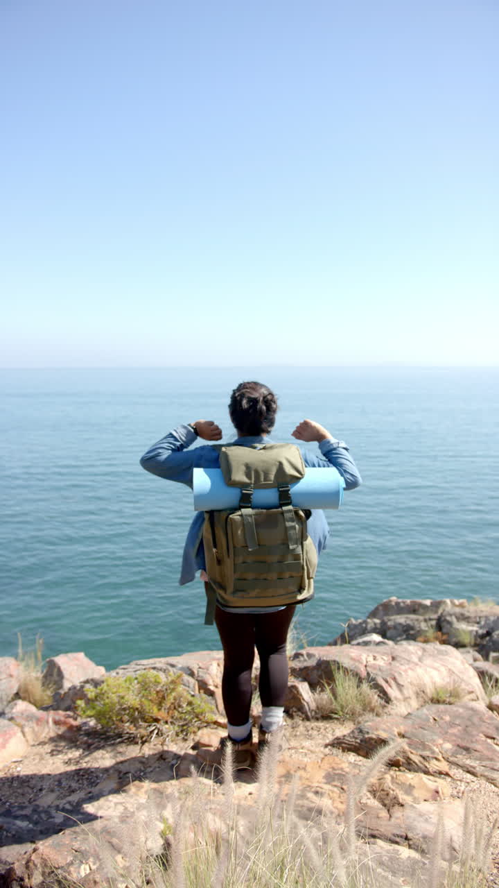 Vertical video: Hiking on mountain, woman with backpack and yoga mat enjoying ocean view