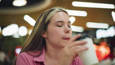 woman in pink dress taking a sip of coffee with a relaxed expression, blurred neon lights in the background, she seems to be enjoying the moment, pausing for a peaceful break