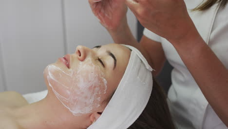 caucasian woman lying back while beautician gives her a facial