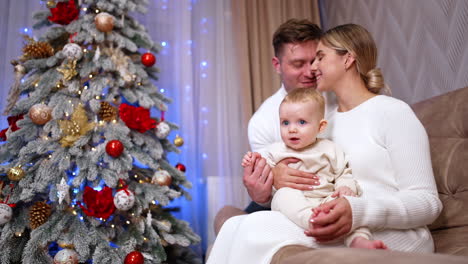 caucasian couple with their infant baby sitting on the sofa. portrait of a happy caucasian family at home for christmas. low angle view.