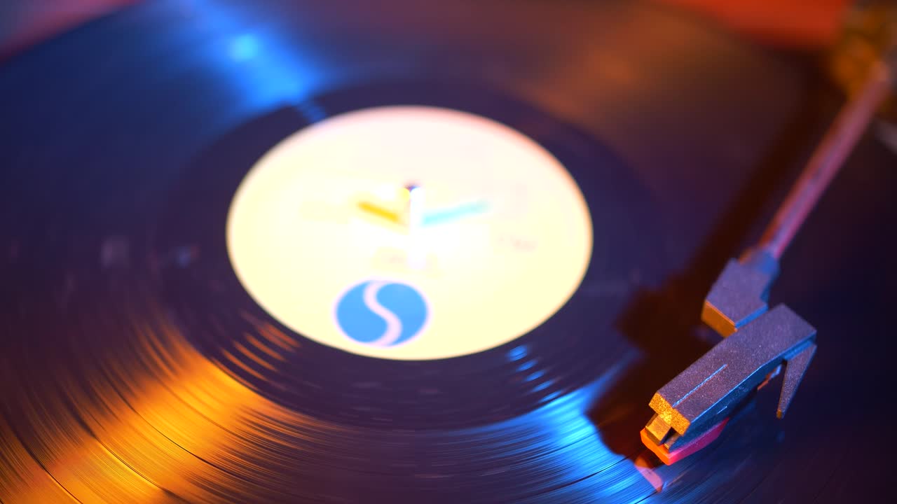 Primo piano di un disco in vinile che gira su un giradischi con luci al neon colorate.