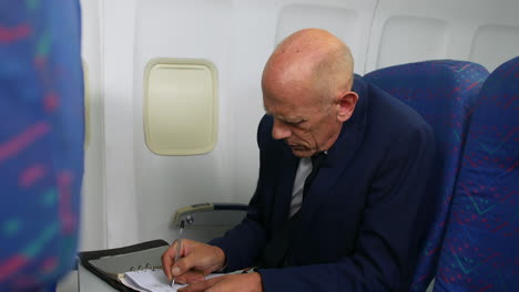 a mature business man working writing in a notebook on an airliner airplane close