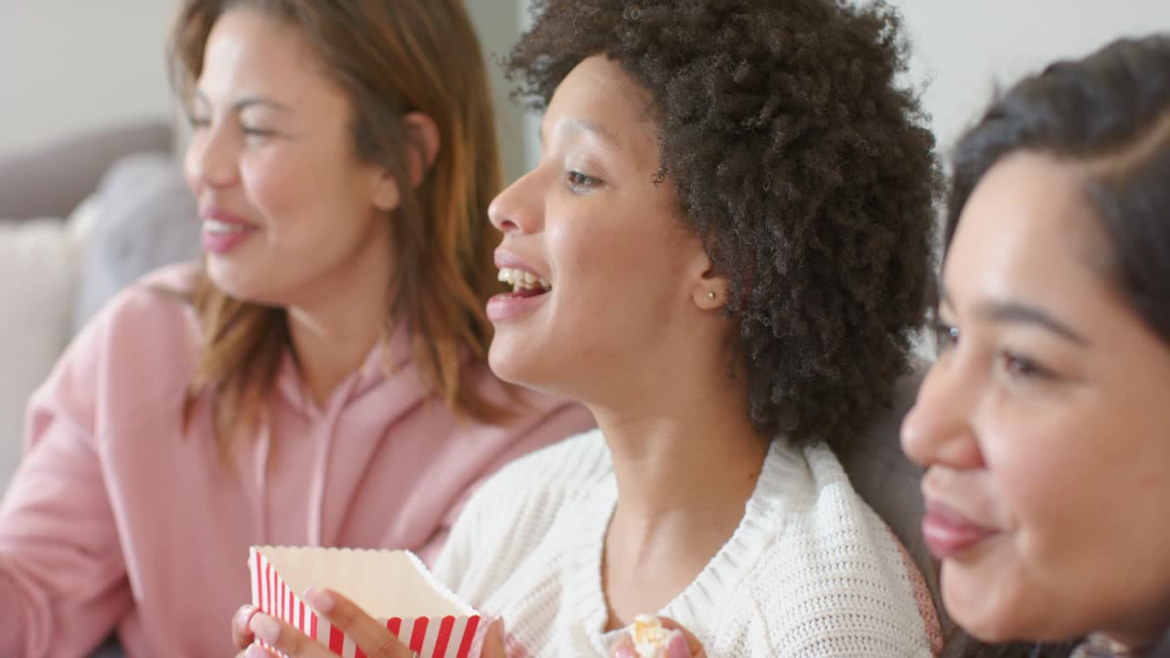 Diverse amiche che reagiscono a una scena fuori campo a casa, mentre condividono popcorn e si concentrano sull'azione