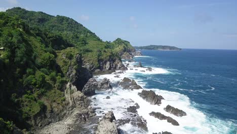 drone shot of rocky coastline with crashing waves on the beach during sunny day