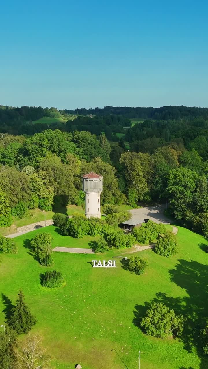 Aerial view revealing Talsi city landmark, water tower standing amid verdant park landscape, showcasing scenic Latvian urban environment with green surroundings