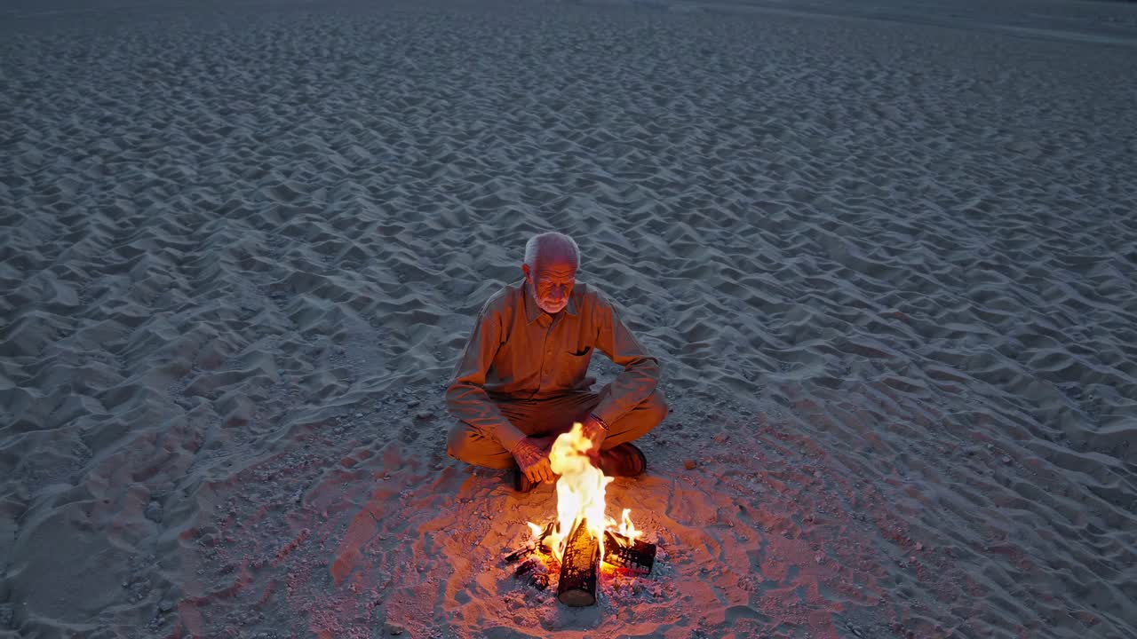 hombre anciano sentado junto a una fogata en el desierto