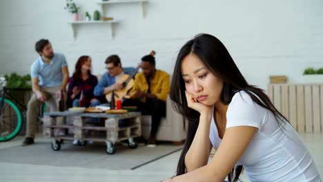 young asian girl feels upset and isolated while her flatmates celebrating party at home indoors