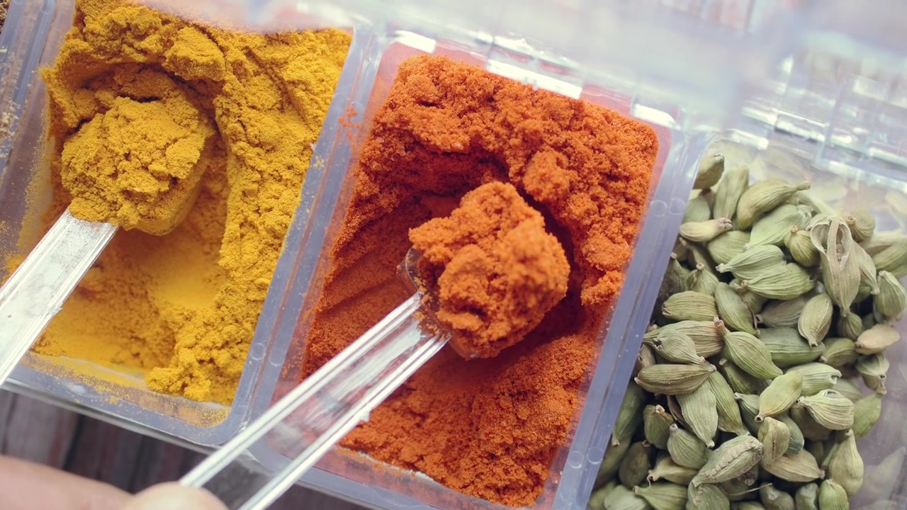 Hand Scooping Red Chili Powder from a Spice Container