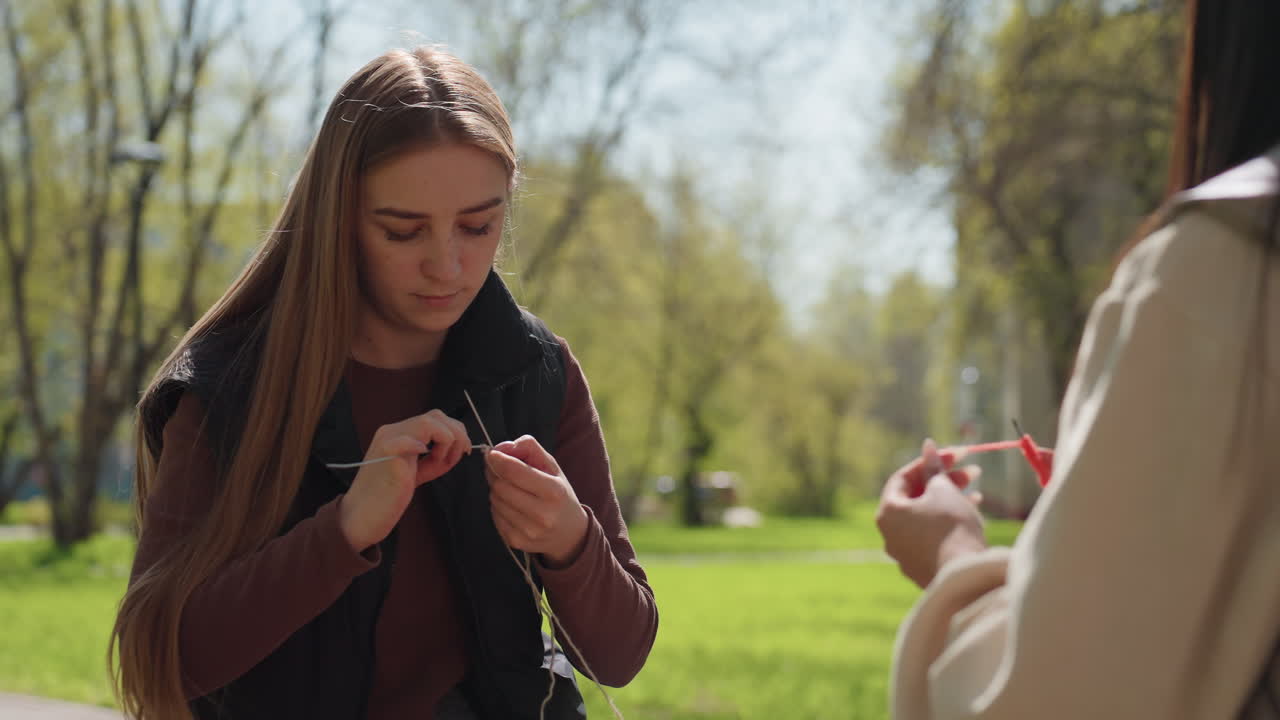 Молодой кавказский пассажир по пути на работу поправляет наушники на тропинке в парке, его руки распутывают провод, смартфон лежит без дела, на нем повседневное пальто, пятнистый солнечный свет, выражение терпения, городской зеленый фон, случайная деталь