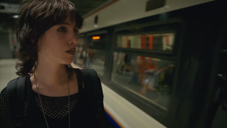 fashion shot of alternative style woman standing on platform of london underground tube station as train leaves shot in real time