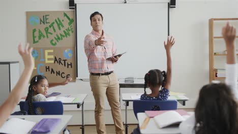 diverse children raising hands and male teacher with tablet in elementary school class, slow motion