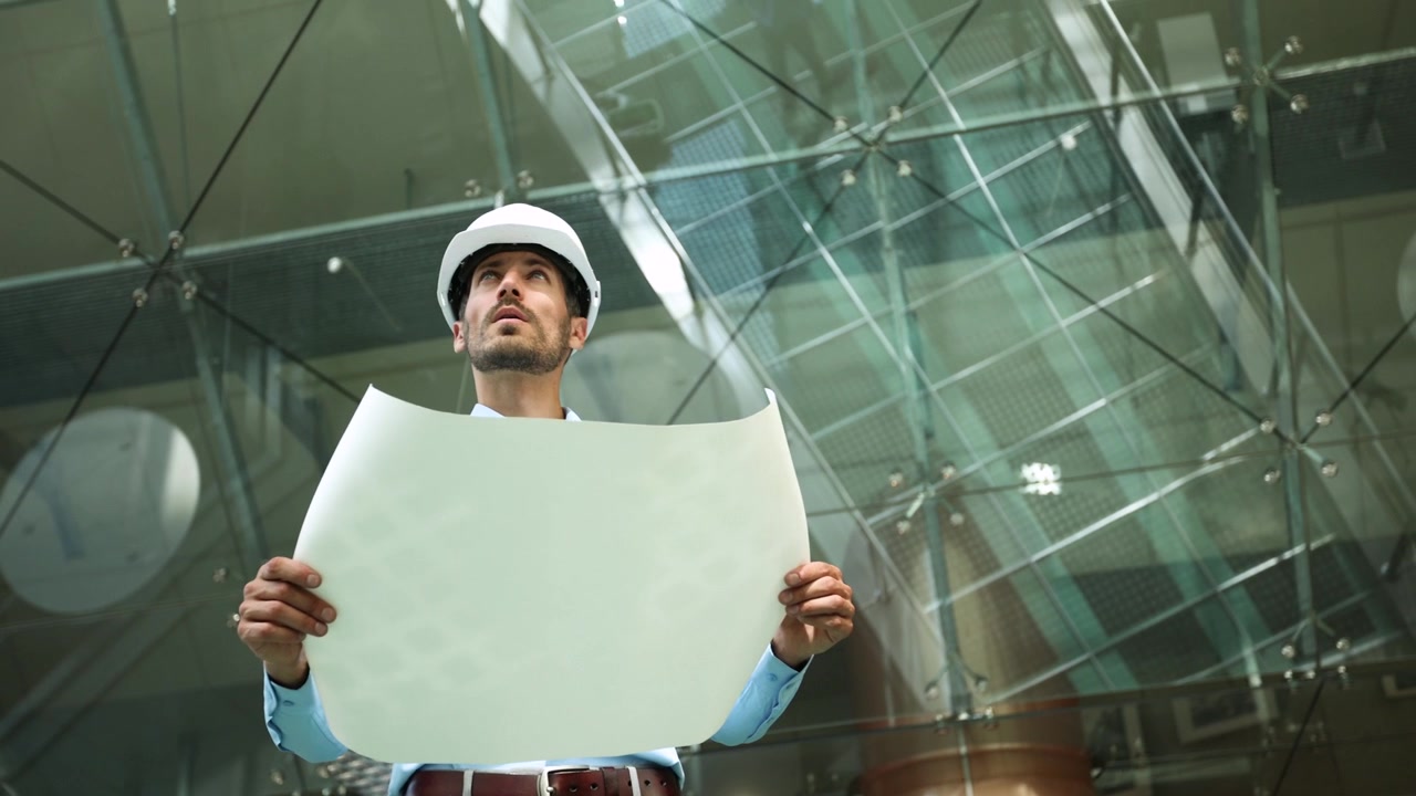 Ingeniero con casco examinando planos en un edificio moderno.