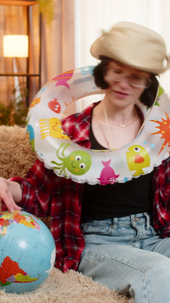 Woman planning beach vacation at home with inflatable swim ring holding globe and airplane tickets