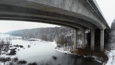 drone shot flying under a bridge in missouri over a frozen lake in a snowstorm