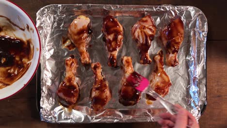 brushing barbecue over chicken legs on tin-foiled pan top view