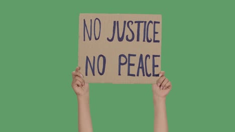 female hands hold a poster from a cardboard box with the words no justice no peace. protest against racism and police brutality. isolated a green screen, chroma key. close up. slow motion