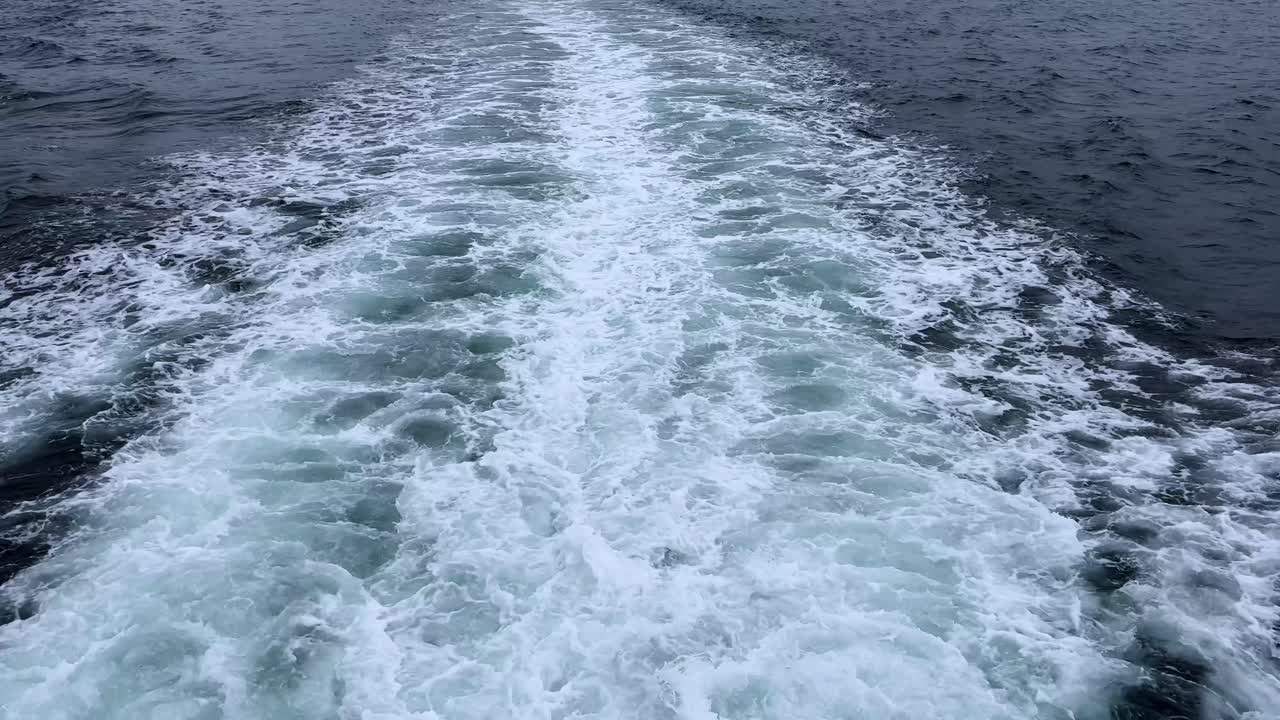 Boat wake trailing across deep blue ocean waters on a cloudy day, creating foamy white patterns