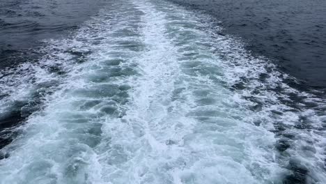 boat wake trailing across deep blue ocean waters on a cloudy day, creating foamy white patterns