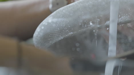 close-up of hands rinsing a metal strainer under a stream of water from the faucet