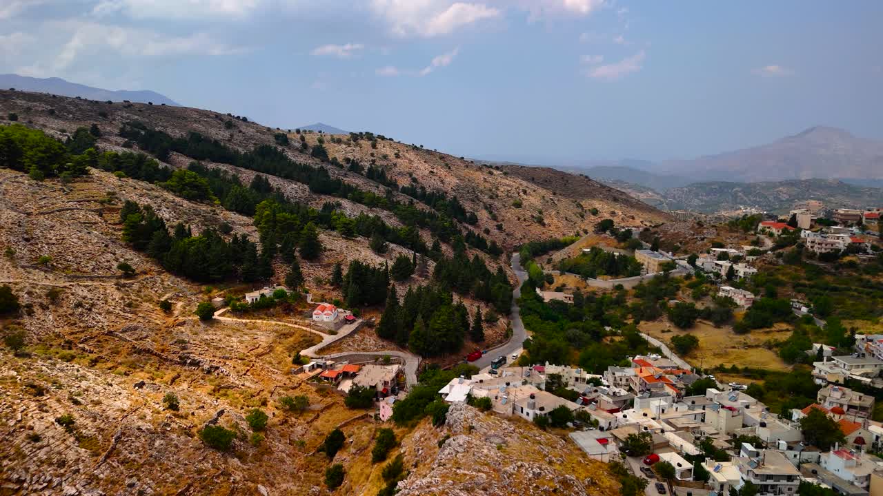 Explore the stunning landscape featuring green mountains and a quaint village nestled in the hills of Greece on a sunny summer day. Experience the beauty of nature and local architecture
