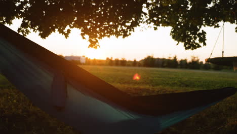 short-haired woman lays down in a hammock as the sun sets at golden hour in the background