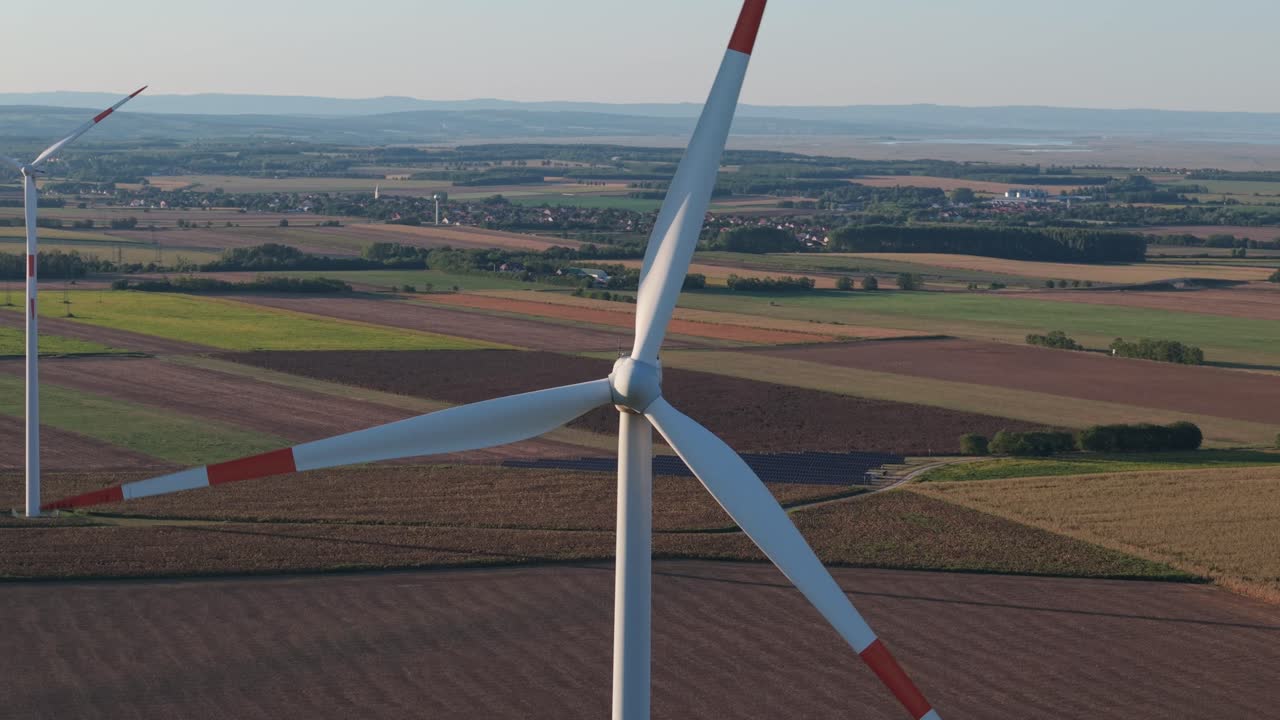 A close-up aerial view of a large wind turbine standing in the middle of colorful agricultural fields