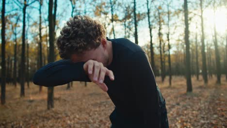 un hombre cansado con el cabello rizado en un uniforme deportivo negro corre a su destino limpia el sudor de su frente y mira a la hora de su carrera por la mañana en el bosque de otoño en una mañana soleada